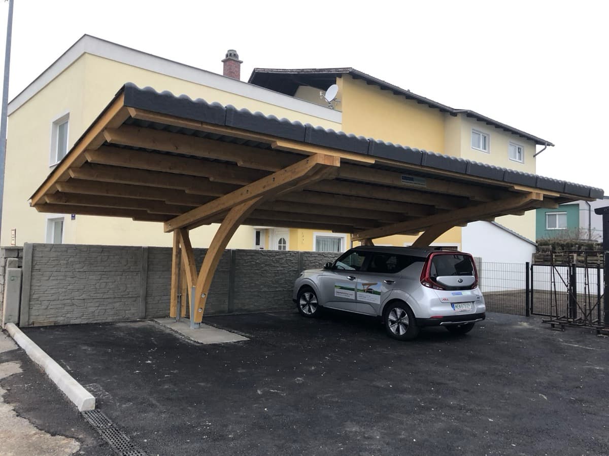 Freistehendes Holz-Carport mit Bogenstützen vor gelbem Haus