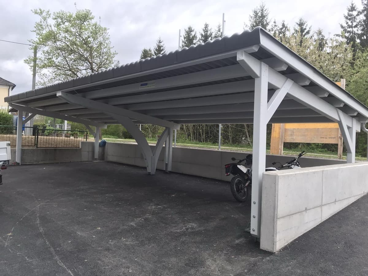 Grauer Metall-Reihencarport mit Bogenstützen und Betonmauer