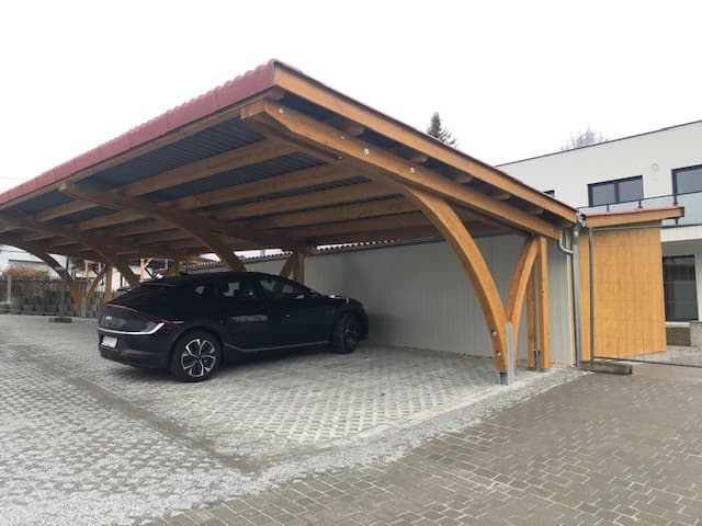 Doppelcarport mit Holzbogen und rotem Blechdach neben Wohnhaus