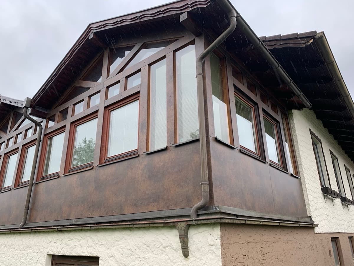 Balkonverkleidung in dunklem Holz mit Fenstern